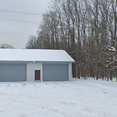 Snow-covered building near forest, green recycling bins nearby.